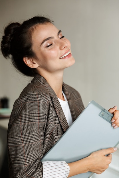 Photo of a pretty positive young business woman indoors at home holding clipboard.