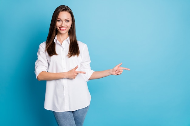 Photo of pretty sales manager lady direct fingers side empty space wear white shirt jeans isolated blue color background