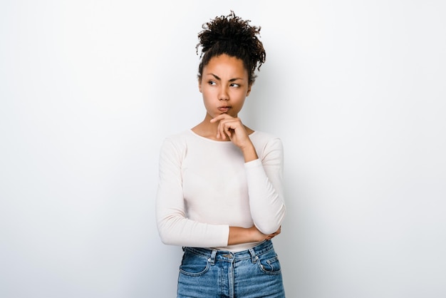 Photo of pretty serious dark skin wavy lady wearing white shirt touching with arm to her chin and looking at the empty space isolated at white colour background