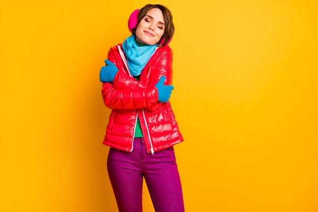 Photo of pretty traveler lady enjoy warm coat in cold frosty weather hug herself wear stylish casual short red overcoat blue scarf gloves earmuffs pants