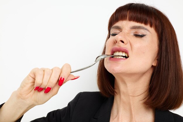 Photo pretty woman in a black jacket a knife and a fork near the face light background