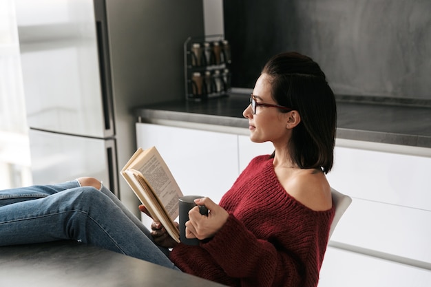 Photo of a pretty woman indoors in home at the kitchen reading book.