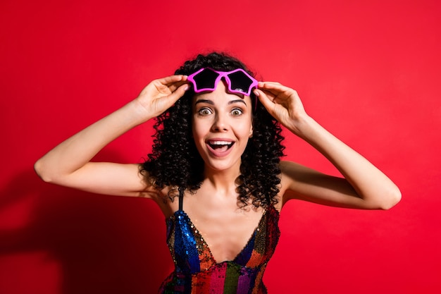 Photo of pretty young girl hold specs excited face wear star-shaped sunglass glossy dress isolated bright red color background