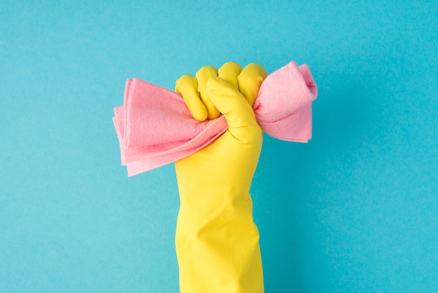 Фотография поднятой руки в желтой перчатке, сжимающей розовую тряпку в кулак на изолированном синем фоне с копирайтом
