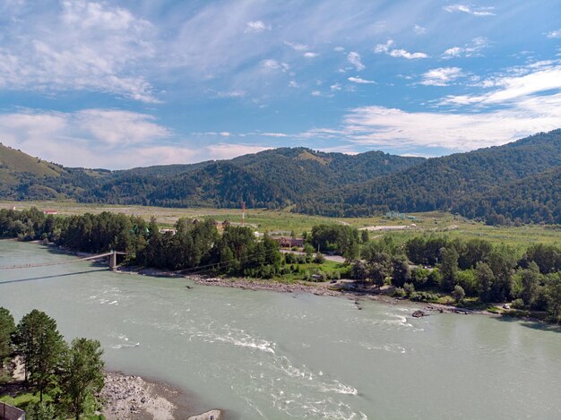 A photo of the recreation center taken from a drone. Picturesque rocky mountains under a sunny blue sky, a flowing river and several houses. Outdoor recreation.