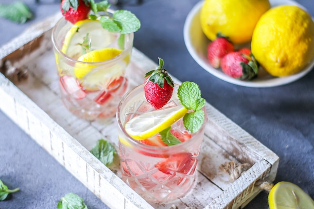 Foto della bevanda fredda ghiacciata di estate rinfrescante con la limonata della menta del limone della fragola in vetro. acqua minerale con fragole fresche e limone. acqua disintossicante con menta e limone e fragola. copia spazio. scatola di legno