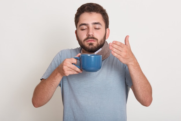 青いマグカップを押し、臭いがしてお茶やコーヒーを飲んでリラックスした若い男の写真。