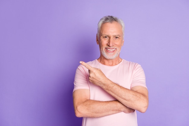 Photo of retired grandpa indicate forefinger empty space wear pink t-shirt isolated purple color background