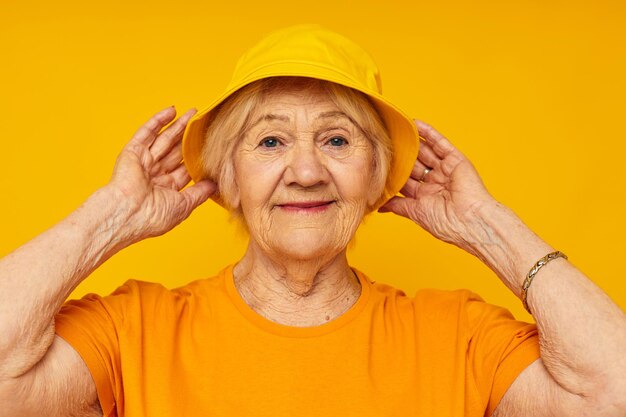 Photo of retired old lady in yellow tshirts hat posing isolated background