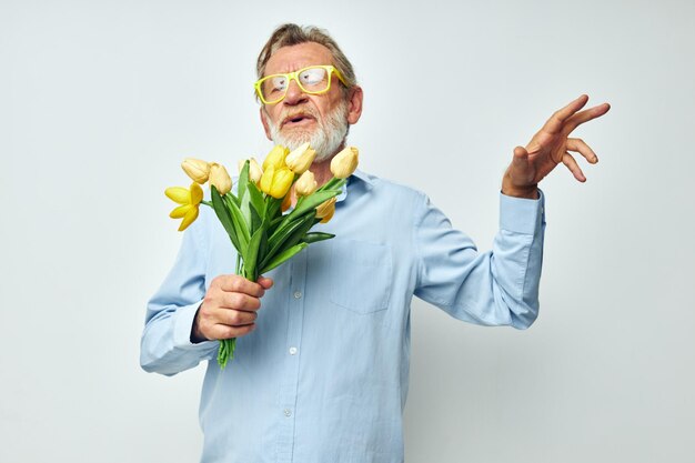 Photo of retired old man in a blue shirt with a bouquet of flowers light background