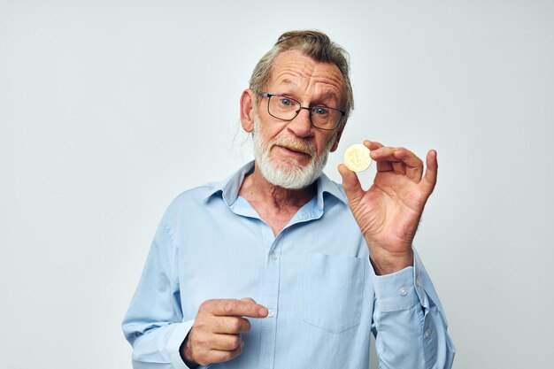 Photo of retired old man in blue shirts bitcoin in hands light background