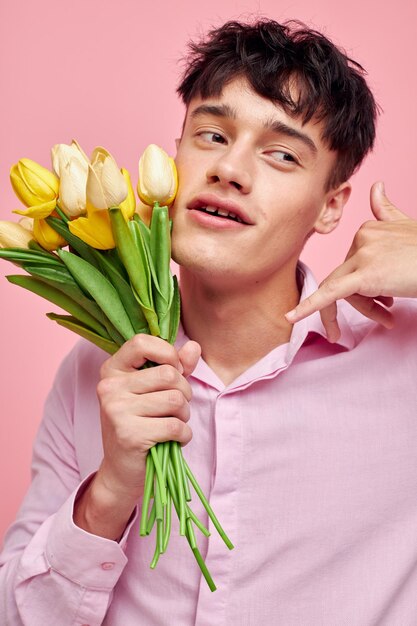 핑크 셔츠를 입은 낭만적인 젊은 남자 친구의 사진, 꽃다발을 들고 손으로 몸짓을 하는 모습