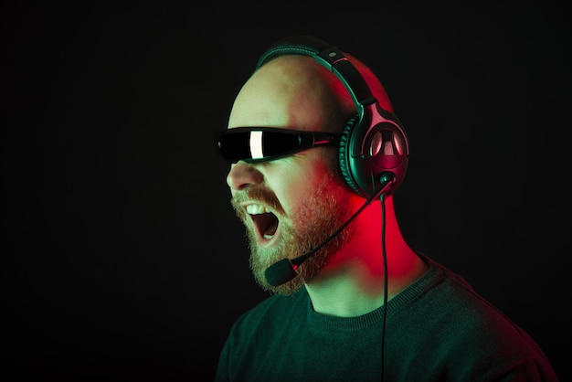 Photo of a screaming bearded man wearing cyclops glasses and headphones over dark background with red and green light