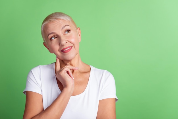 Photo of senior woman finger touch chin wondered look empty space thoughtful isolated over green color background.