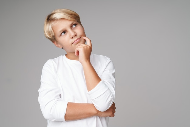 Photo of a serious thoughtful blonde boy child posing isolated over grey wall.