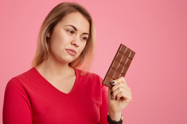 Photo of serious woman holds bar of cocoa chocolate