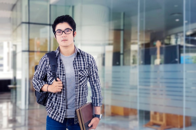 Photo of serious young male student standing in front of glass door