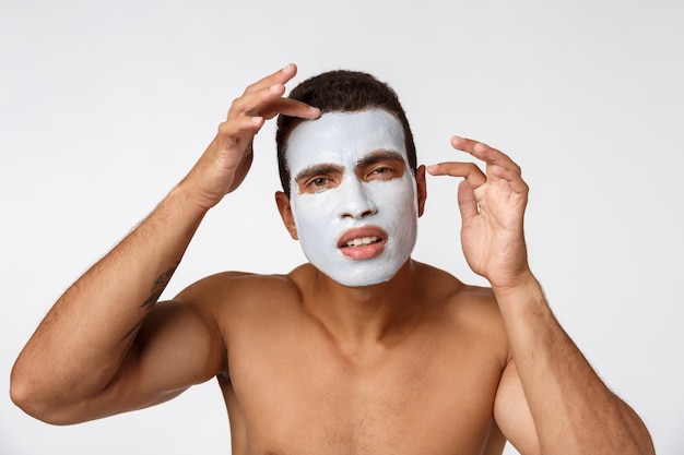 Photo of shirtless man smiling and applying face cream isolated over white