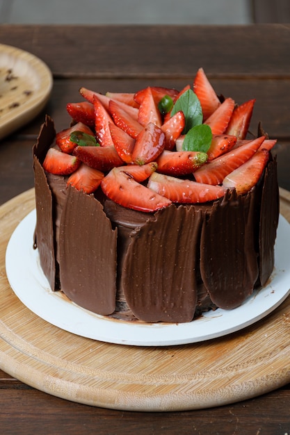 Photo shoot with chocolate cake being decorated. Chocolate cake covered with strawberries, fresh basil leaves, blackberry jam and chocolate plates around.