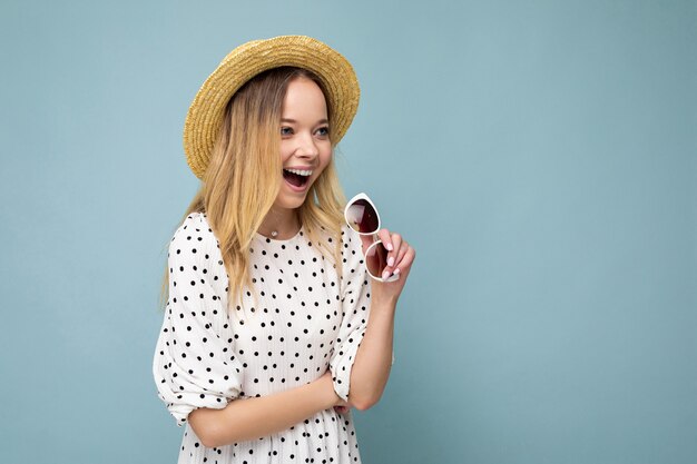 Photo shot of attractive happy smiling young blonde woman wearing summer casual clothes and stylish sunglasses isolated over colorful background wall looking to the side