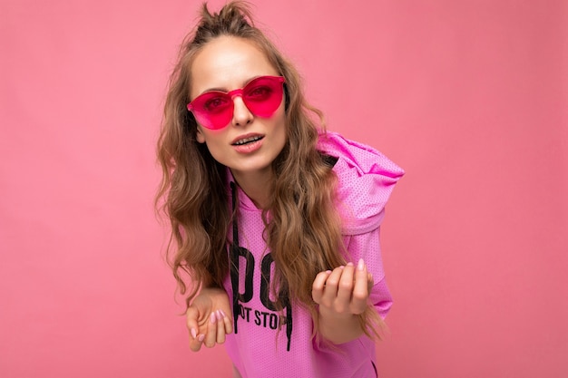 Photo shot of beautiful asking young dark blonde woman wearing casual clothes and stylish sunglasses