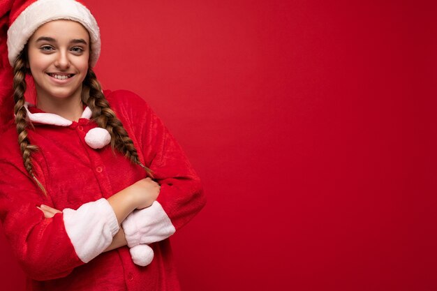 Foto scatto fotografico di una bella ragazza bruna sorridente positiva felice con le trecce che indossa abiti con clausola di babbo natale