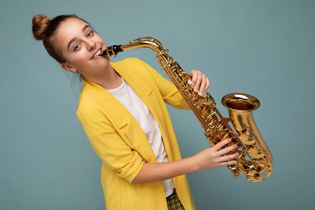 Scatto fotografico di una bellissima bambina bruna sorridente felice che indossa una giacca gialla elegante in piedi