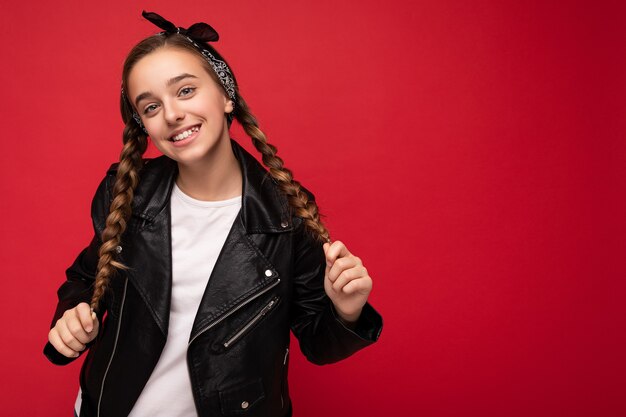 Foto scattata di bella bambina bruna sorridente felice con le trecce vestita di nero alla moda