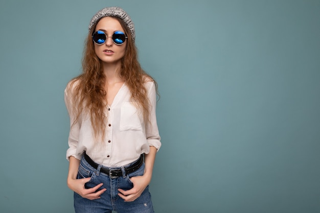 Photo shot of beautiful positive young blonde woman wearing casual clothes and stylish optical glasses isolated over colorful background wall looking at camera. free space