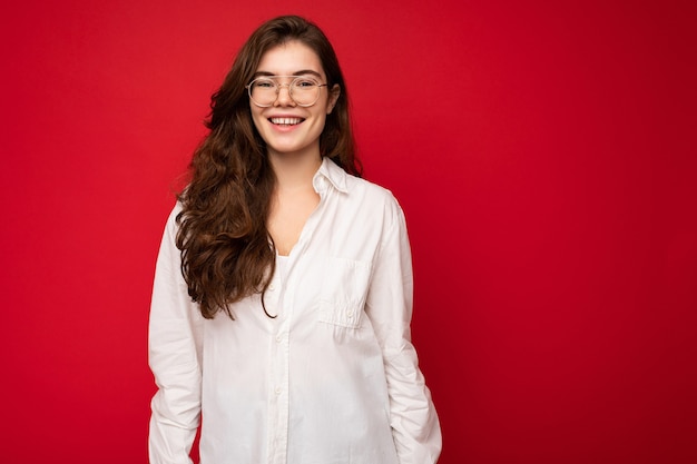 Photo shot of beautiful positive young brunette woman wearing casual clothes and stylish optical glasses isolated over colorful background wall looking at camera. empty space