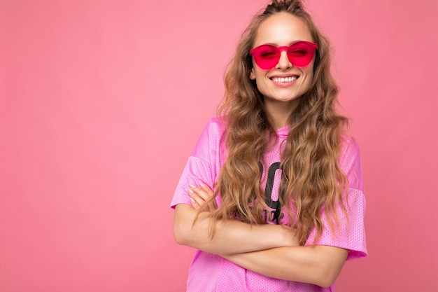 Photo shot of beautiful smiling happy young dark blonde woman wearing casual clothes and stylish sunglasses isolated over colorful wall . copy space