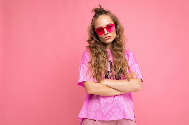 Photo shot of beautiful young dark blonde woman wearing casual clothes and stylish sunglasses