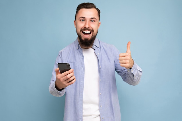 Photo shot of positive handsome bearded good looking young man wearing casual stylish outfit poising