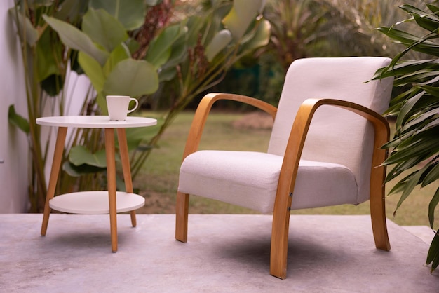 Photo shows purple upholstered chair and table with cup of\
coffee on terrace in patio near green tropical garden still life\
concept