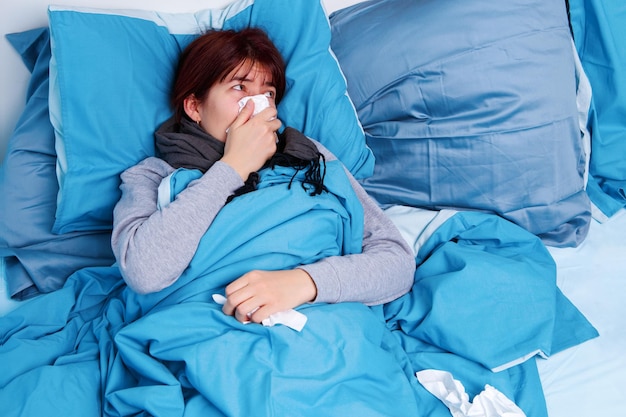 Photo of sick brunette blowing her nose in paper handkerchief lying in bed