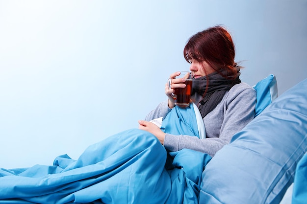 Foto di bruna malata con una tazza di tè seduta a letto