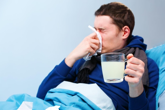 Photo of sick man in scarf with cup of medicine lying in bed