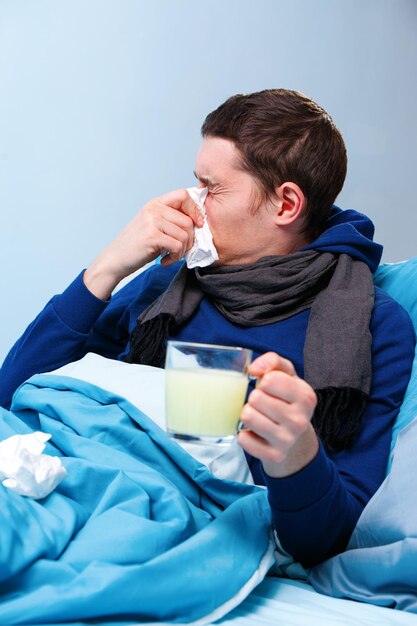 Photo of sick man in scarf with cup of medicine lying in bed