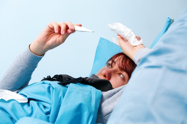 Photo of sick woman with thermometer lying on bed