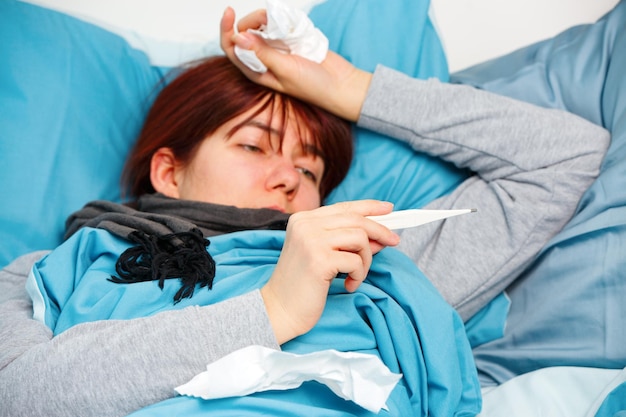 Photo of sick woman with thermometer lying on bed