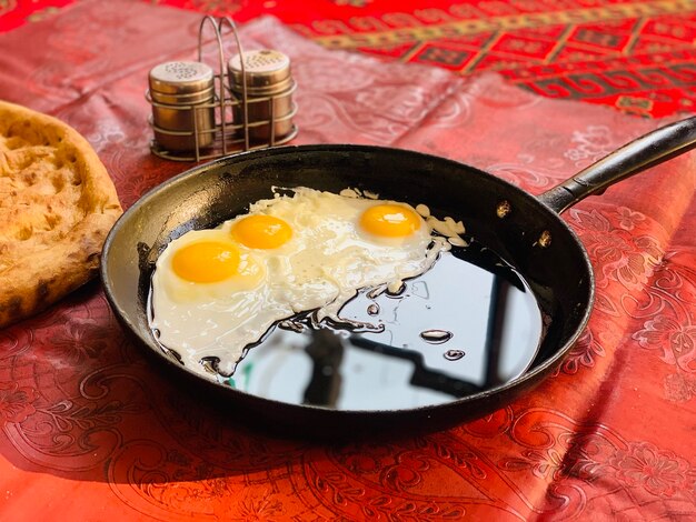 Photo photo side view of fried eggs in a pan with bread on red carpet