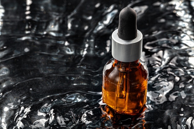 Photo of skincare serum bottle in black wavy water close up