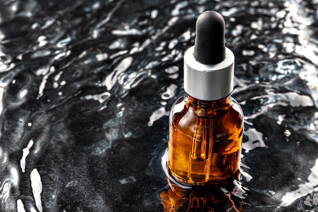 Photo of skincare serum bottle in black wavy water close up