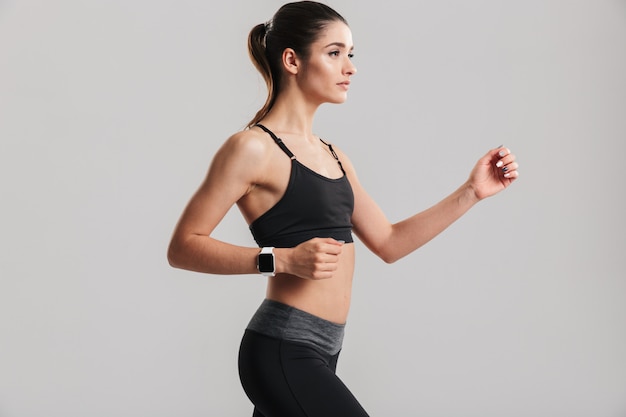 Photo of slim fitness woman running or working out with watch on wrist, isolated over gray wall