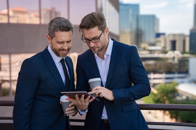 Photo of smiling businessmen check business report outdoor on tablet