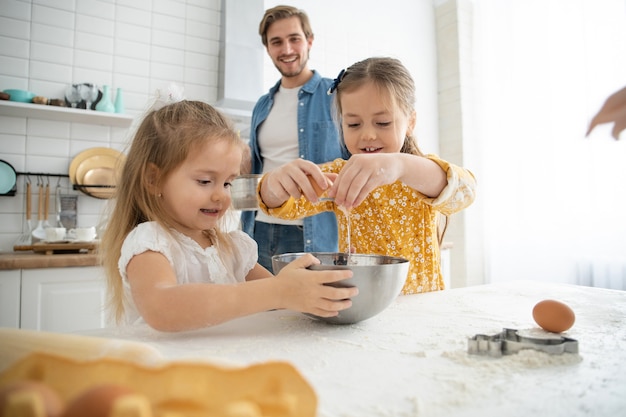 Фотография улыбающегося отца и дочерей, которые пекут на кухне и веселятся.