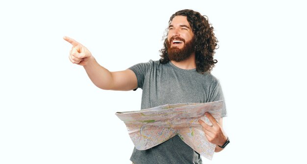 Photo photo of smiling happy bearded man traveller holding map and pointing on the way