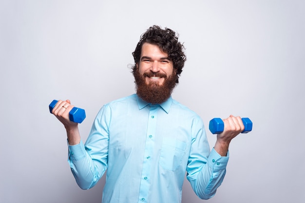 Photo of smiling man in blue shirt holding small dumbbells, fitness concept.