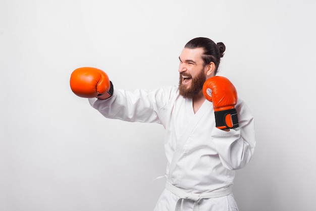 Photo of smiling man in taekwondo uniform training over white wall