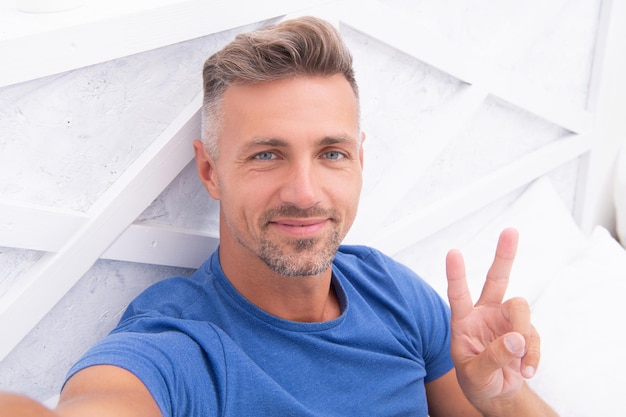 Photo of smiling selfie man with phone at home selfie man with phone in bedroom